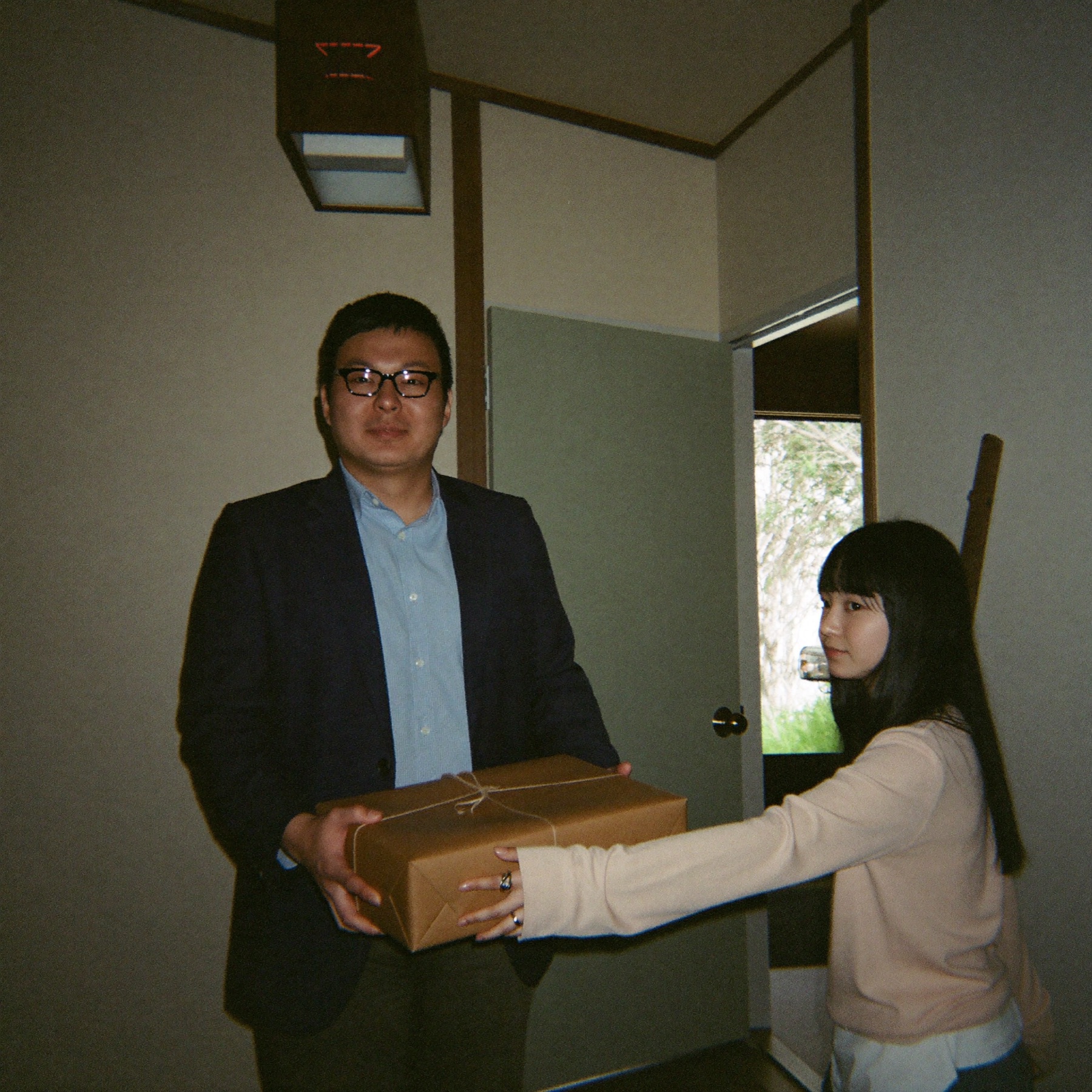 玄関先で包みを渡す娘と受け取る父